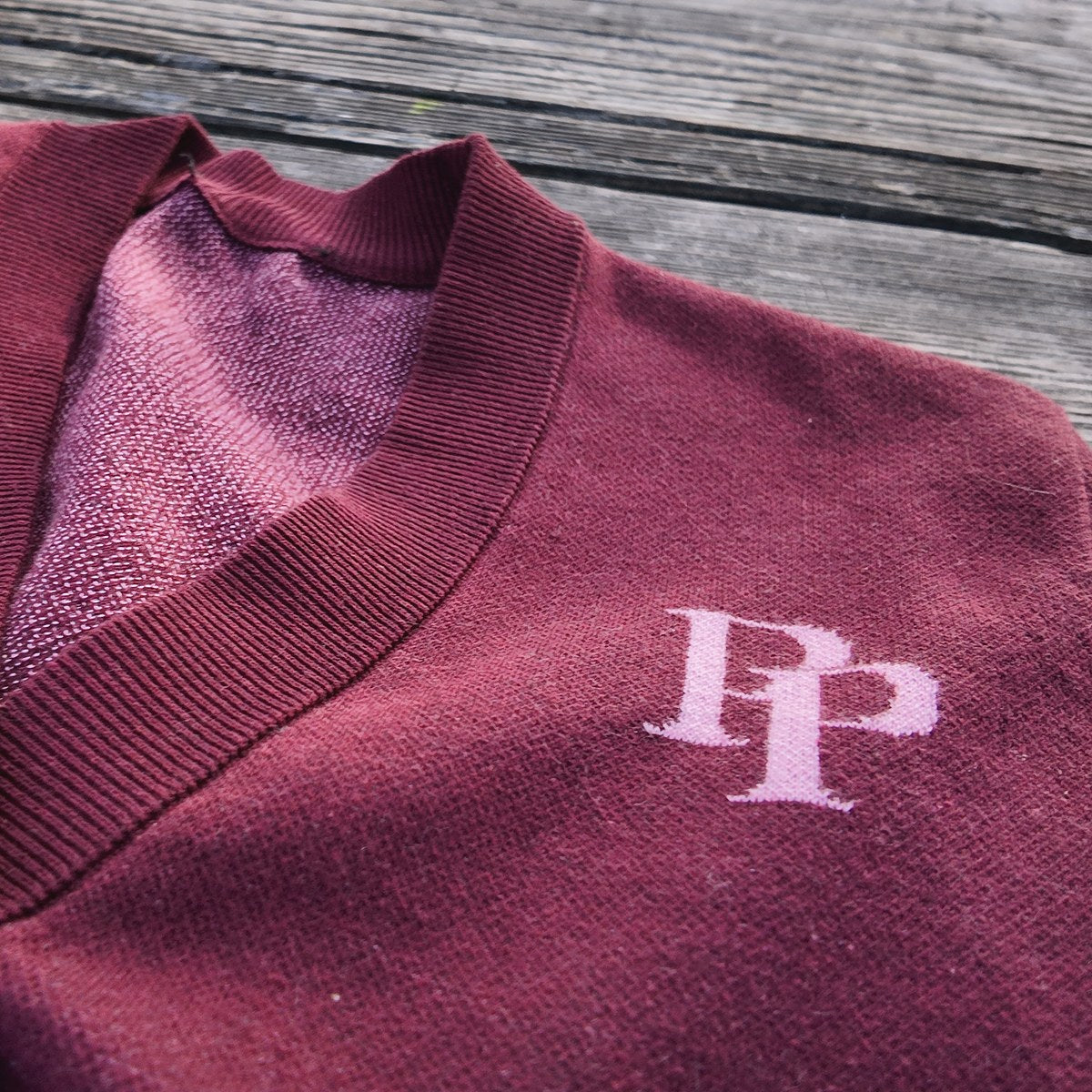A burgundy cardigan with a ribbed V-neck and the rose pink PP monogram