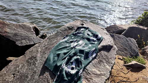 Hunter Green Crest sweater vest and matching dog sweater on a rock by the water