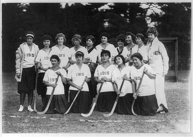 Historic Vassar field hockey team posing with hockey sticks in uniforms marked 1915