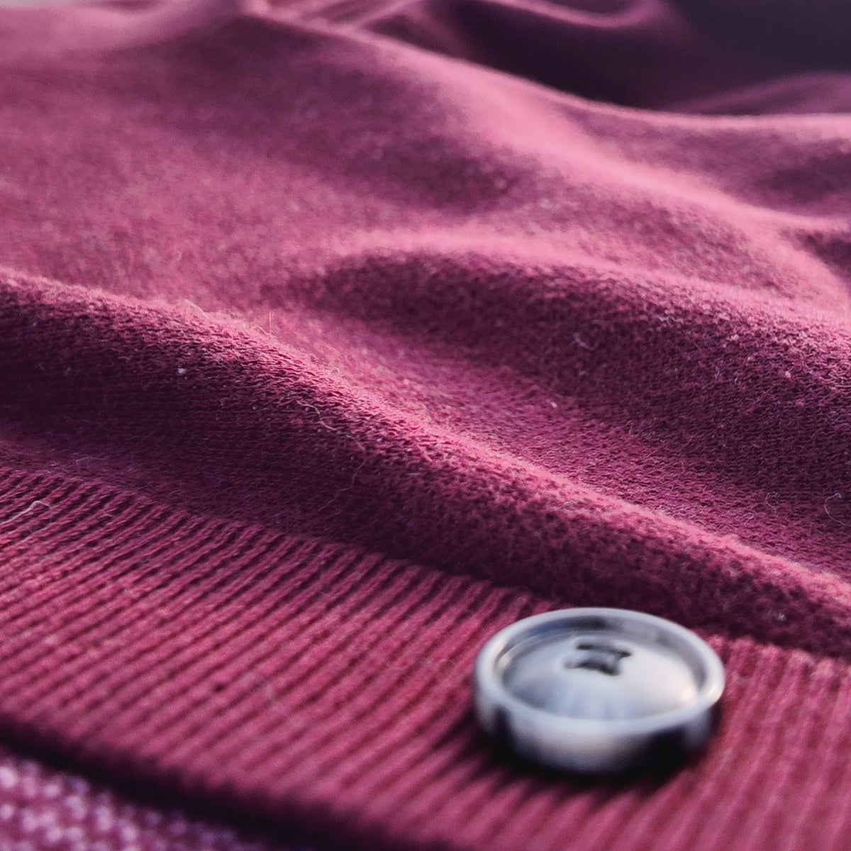 A button on the ribbed placket of a burgundy cardigan