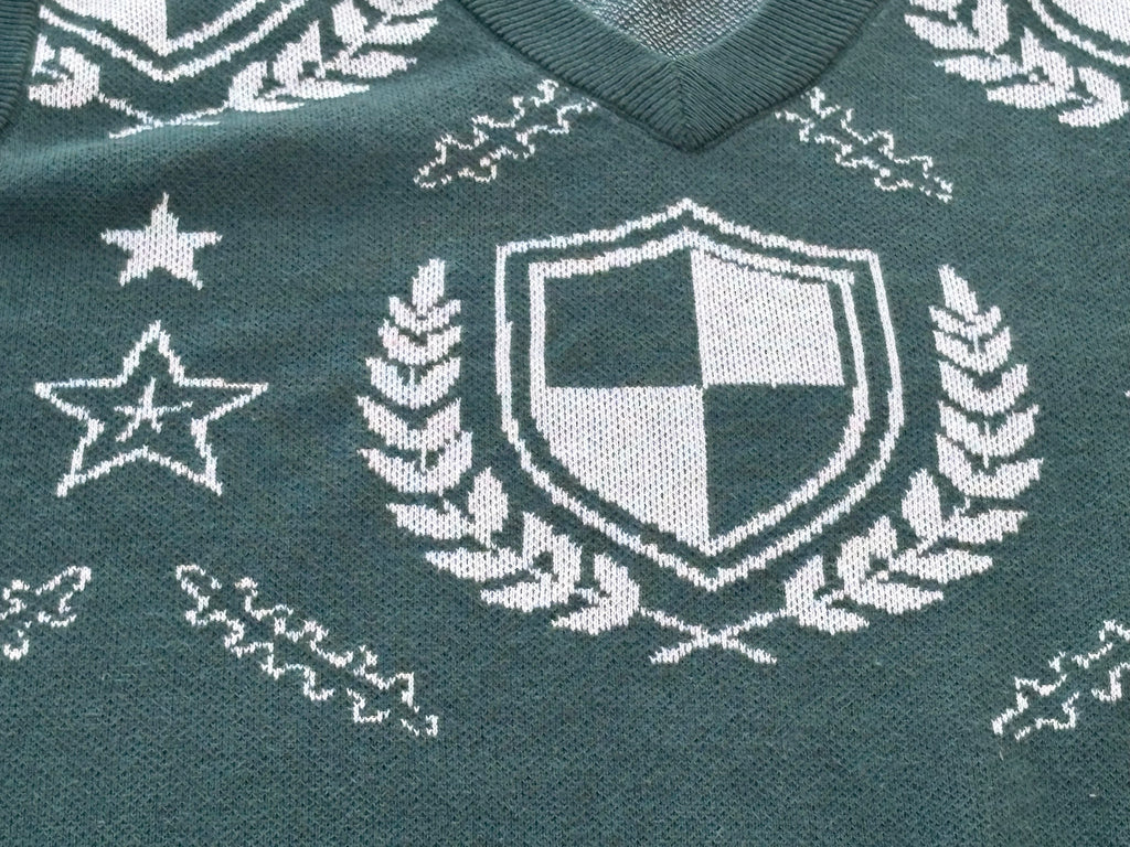 Close-up of the green crest sweater vest: cream shield, laurels and stars in jacquard knit