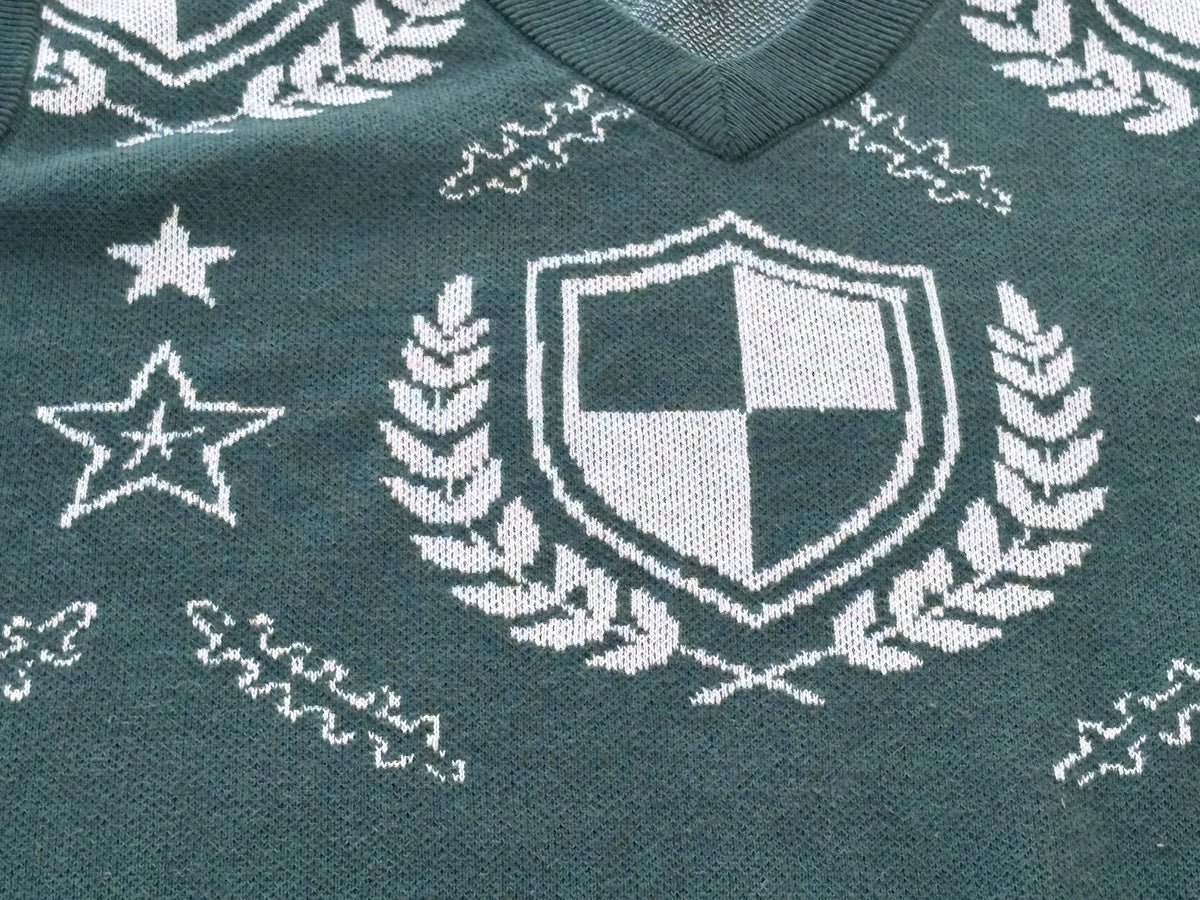 Close-up of the green crest sweater vest: cream shield, laurels and stars in jacquard knit