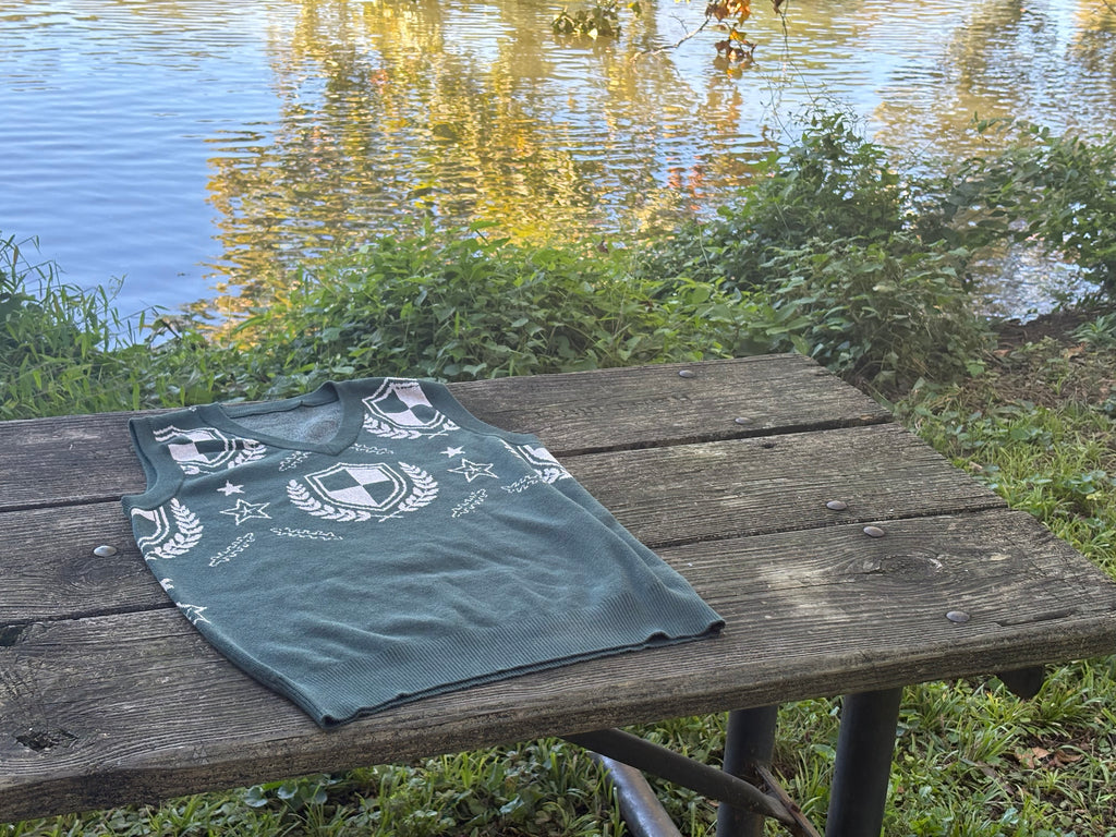 Green crest V-neck sweater vest on a wooden table by the water