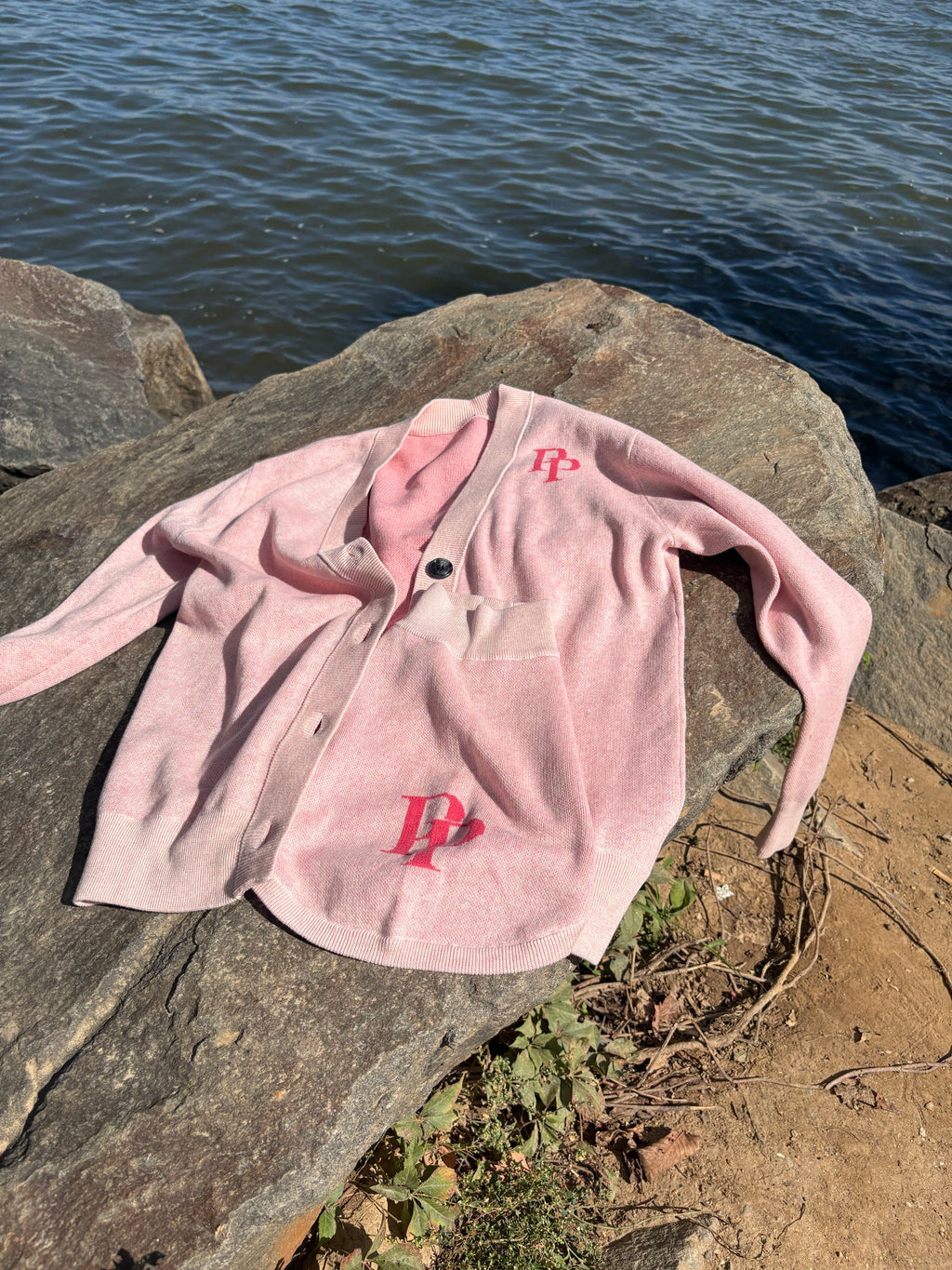 Pink monogram cardigan and matching dog sweater laid on a rock