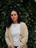 Model wearing the Public Prep Sand & Ivory cardigan over a white tee, in front of green leaves