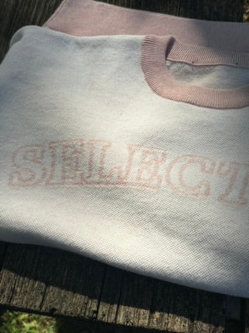 Selective sweater folded to show its pink neckline and wordmark